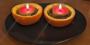 Two candles set in orange halves on a black plate  