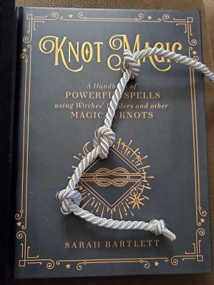 A book called knot magick with a white knotted rope laying across it